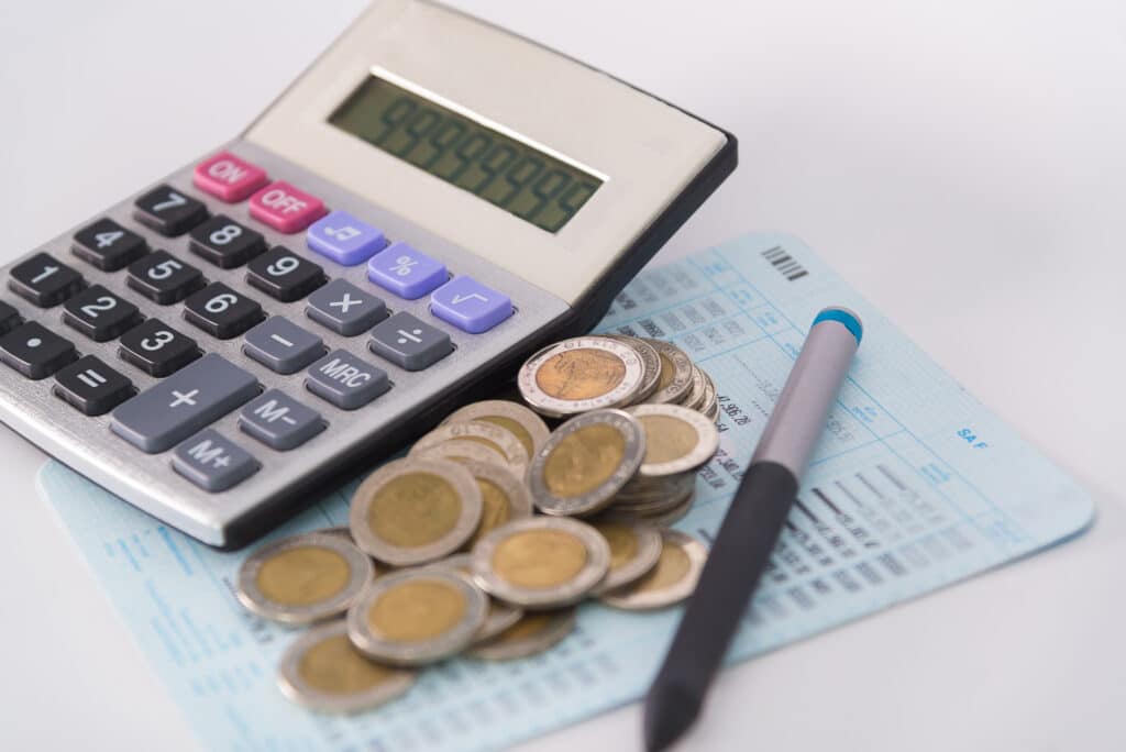 Savings, increasing columns of coins, piles of coins arranged as a graph and calculator with pen on white background, business idea, shallow focus.